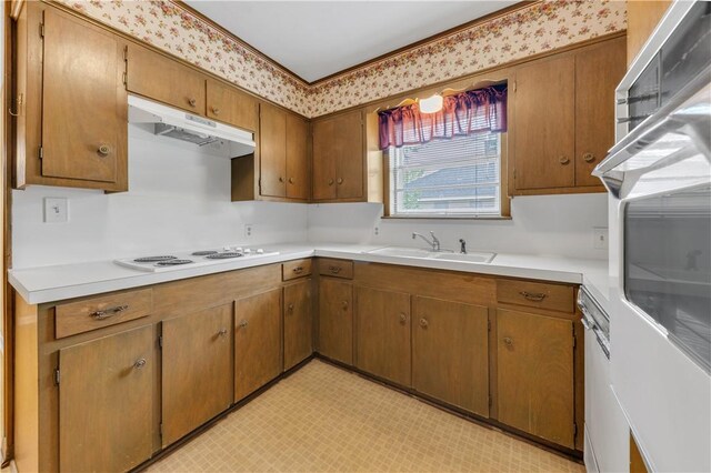 kitchen featuring light countertops, white appliances, under cabinet range hood, a sink, and light floors