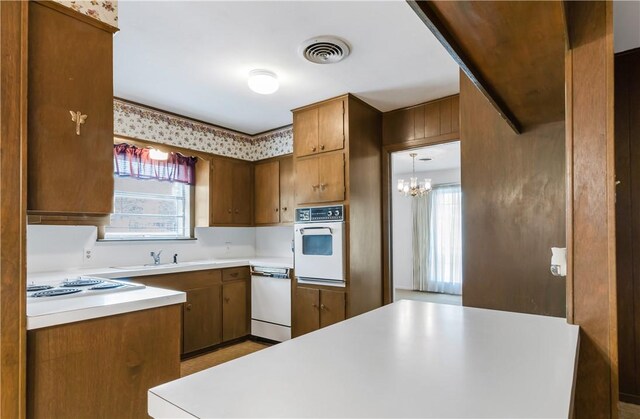 kitchen featuring a notable chandelier, light countertops, a sink, white appliances, and visible vents