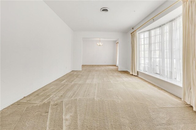 carpeted empty room featuring visible vents and an inviting chandelier