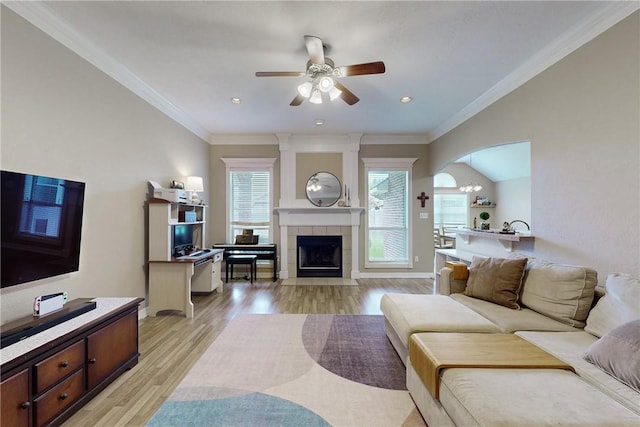 living room with a tiled fireplace, crown molding, light hardwood / wood-style flooring, and ceiling fan with notable chandelier