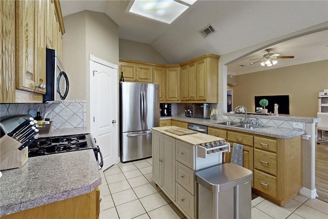 kitchen with sink, vaulted ceiling, decorative backsplash, a kitchen island, and appliances with stainless steel finishes