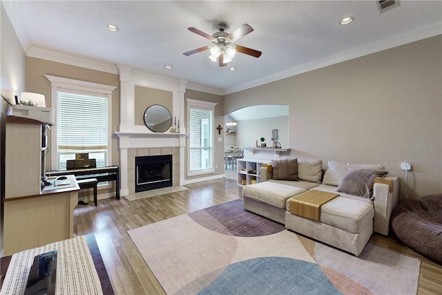 living room with ceiling fan, light hardwood / wood-style floors, crown molding, and a tile fireplace