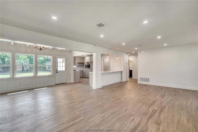 unfurnished living room featuring a chandelier, light hardwood / wood-style flooring, and sink