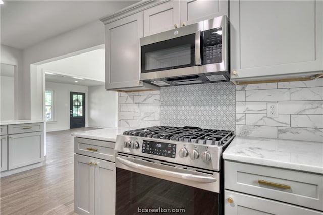 kitchen with decorative backsplash, gray cabinets, light wood-type flooring, appliances with stainless steel finishes, and light stone counters