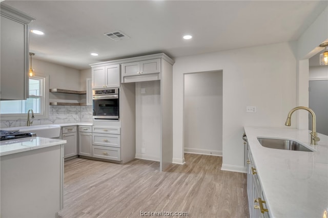 kitchen featuring tasteful backsplash, light stone counters, stainless steel oven, sink, and light hardwood / wood-style flooring