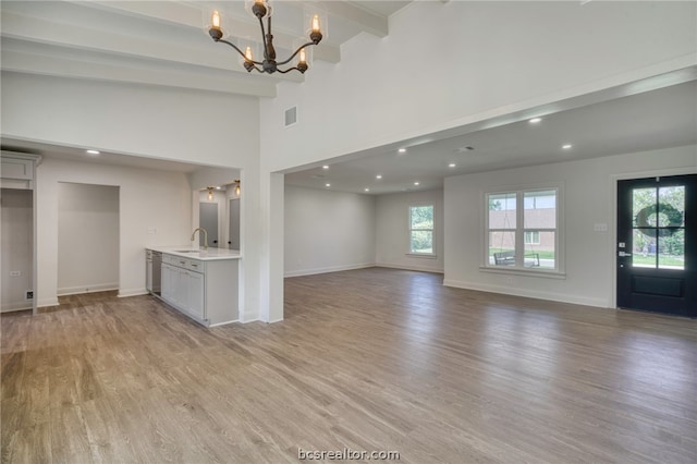 unfurnished living room featuring sink, high vaulted ceiling, an inviting chandelier, beamed ceiling, and light hardwood / wood-style floors