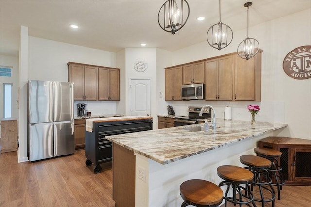 kitchen with light stone countertops, hanging light fixtures, kitchen peninsula, appliances with stainless steel finishes, and light wood-type flooring