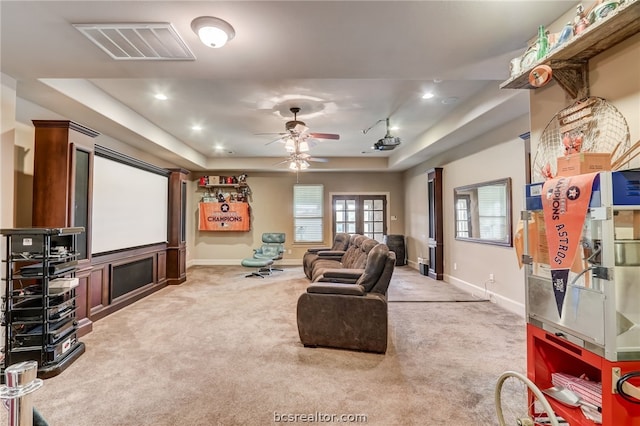 home theater room featuring ceiling fan, carpet floors, and a tray ceiling