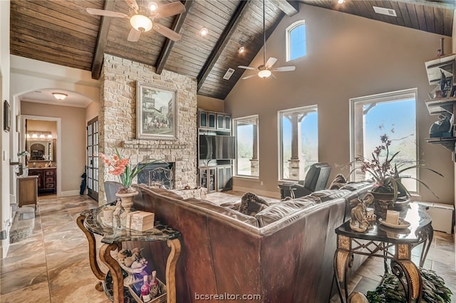 living room with ceiling fan, wooden ceiling, a stone fireplace, beamed ceiling, and high vaulted ceiling