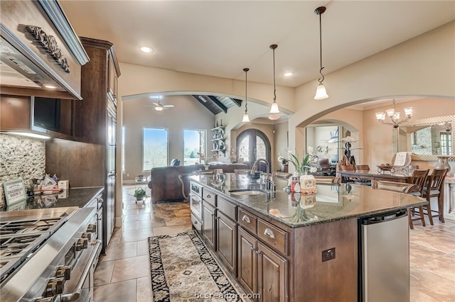 kitchen with sink, dark stone countertops, an island with sink, lofted ceiling, and decorative light fixtures