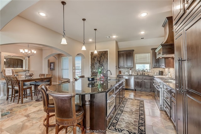 kitchen featuring dark brown cabinets, an island with sink, stainless steel appliances, and decorative light fixtures