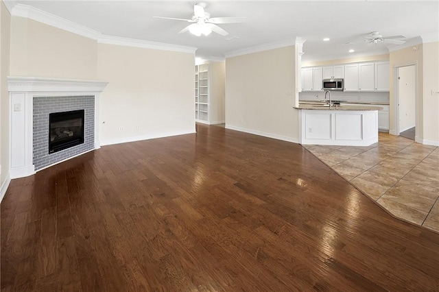 unfurnished living room featuring ornamental molding, hardwood / wood-style floors, a fireplace, ceiling fan, and sink