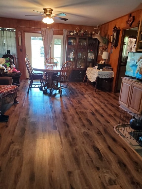 dining room featuring dark hardwood / wood-style flooring, wooden walls, and ceiling fan