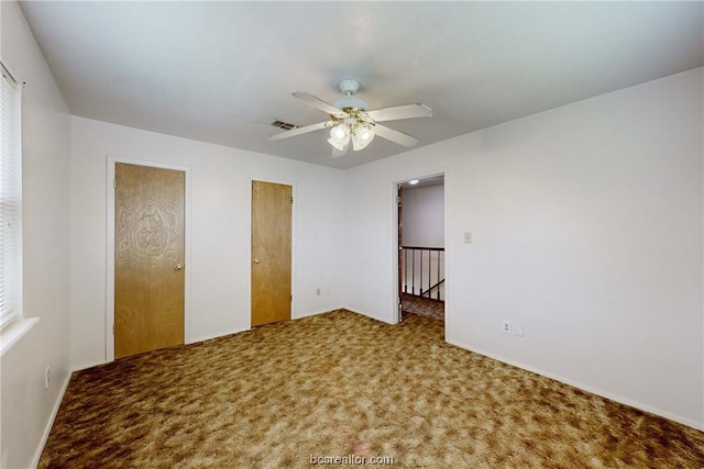 unfurnished bedroom featuring carpet, ceiling fan, and multiple closets