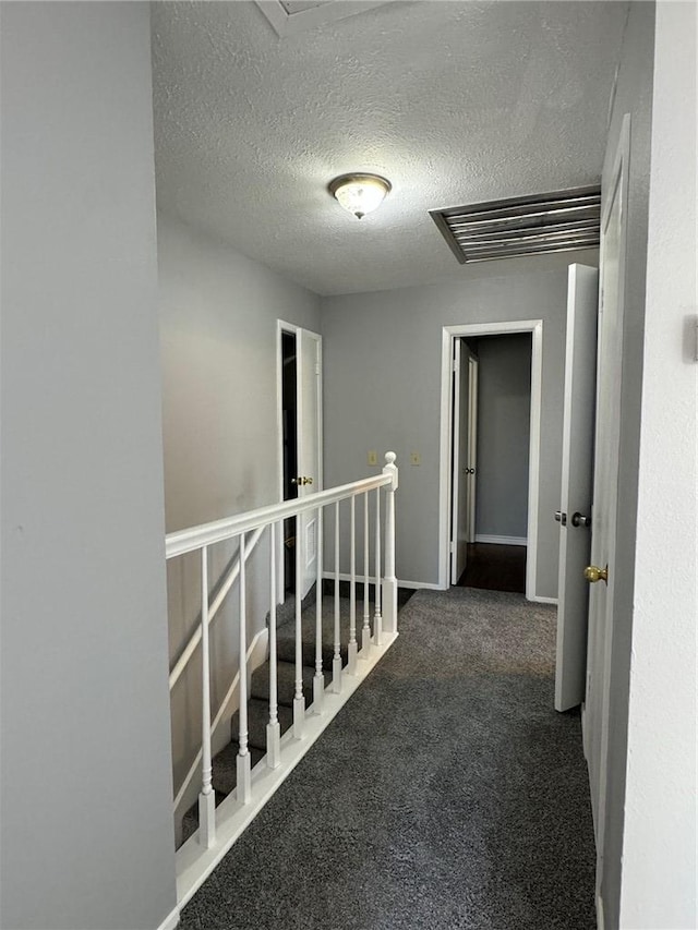 hallway featuring dark colored carpet and a textured ceiling