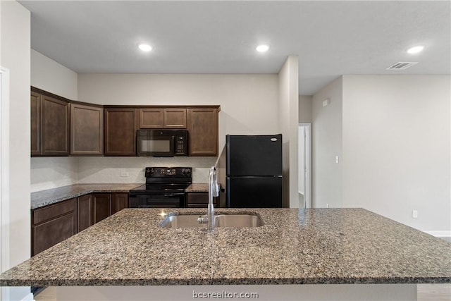 kitchen with light stone countertops, sink, an island with sink, and black appliances