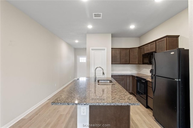 kitchen with black appliances, a center island with sink, sink, and light hardwood / wood-style flooring