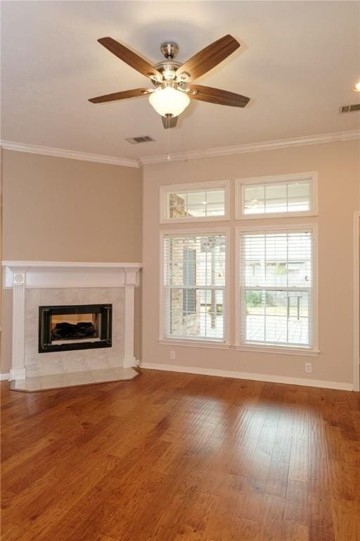 unfurnished living room with a tiled fireplace, crown molding, wood-type flooring, and ceiling fan