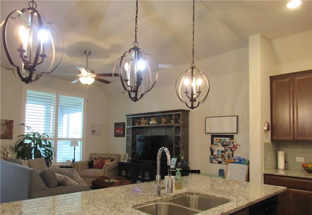 kitchen with a sink, open floor plan, pendant lighting, decorative backsplash, and light stone counters