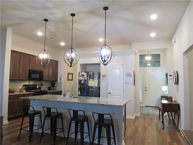 kitchen featuring stone counters, a sink, black appliances, and dark wood finished floors