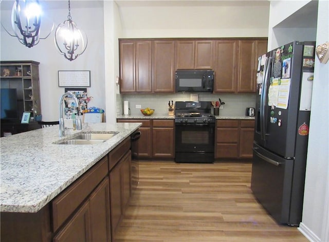 kitchen with an inviting chandelier, backsplash, black appliances, light wood-style floors, and a sink