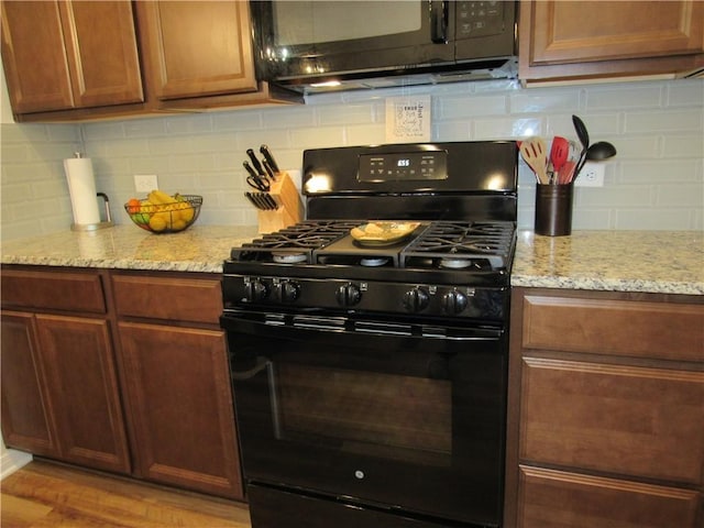 kitchen with tasteful backsplash, light wood-style floors, black appliances, and light stone counters