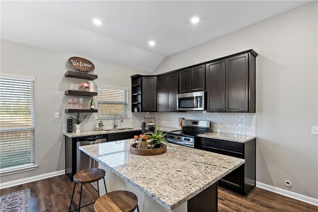 kitchen with appliances with stainless steel finishes, light stone countertops, a kitchen island, and sink