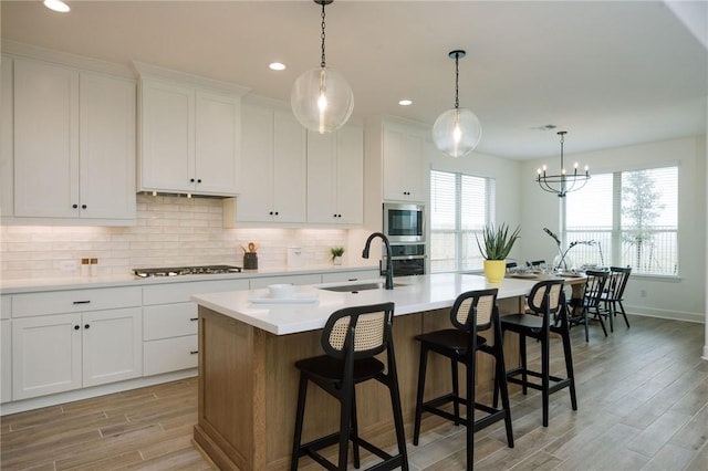 kitchen featuring light wood finished floors, a sink, tasteful backsplash, light countertops, and appliances with stainless steel finishes