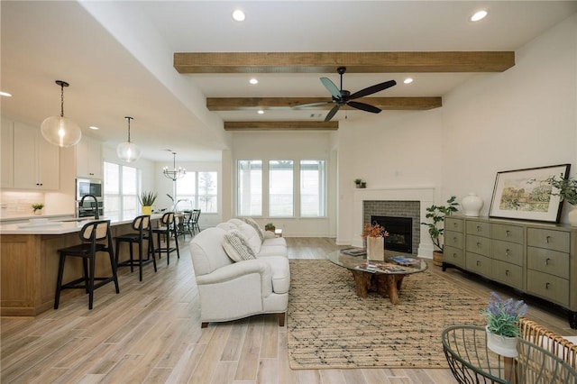 living area with recessed lighting, light wood-style flooring, beamed ceiling, ceiling fan with notable chandelier, and a fireplace