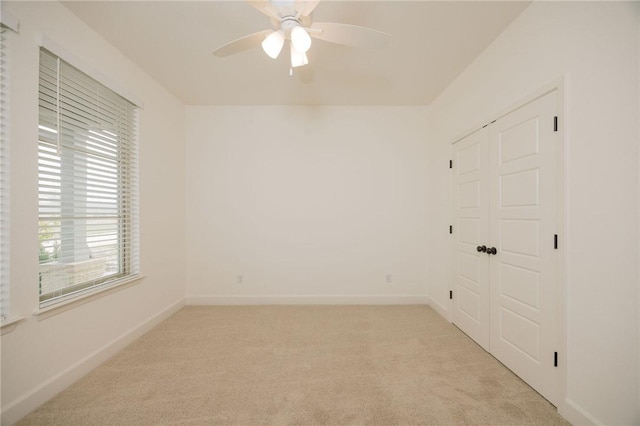 unfurnished room with a ceiling fan, baseboards, and light carpet