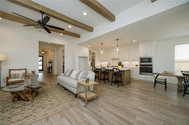 living room with beamed ceiling, light wood finished floors, recessed lighting, a ceiling fan, and baseboards