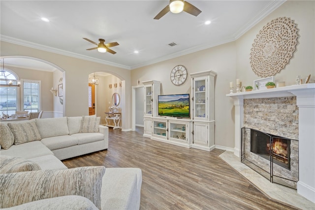 living room with crown molding, a fireplace, ceiling fan with notable chandelier, and hardwood / wood-style flooring