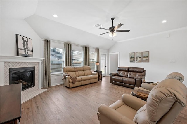 living room with vaulted ceiling, ceiling fan, crown molding, light hardwood / wood-style floors, and a tiled fireplace