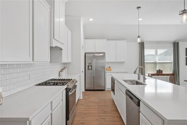 kitchen with white cabinetry, sink, hanging light fixtures, stainless steel appliances, and an island with sink