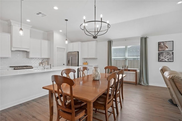 dining space with crown molding, hardwood / wood-style floors, a notable chandelier, and sink