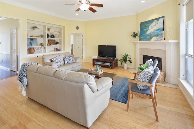 living area featuring ceiling fan, a fireplace, built in features, ornamental molding, and light wood-type flooring