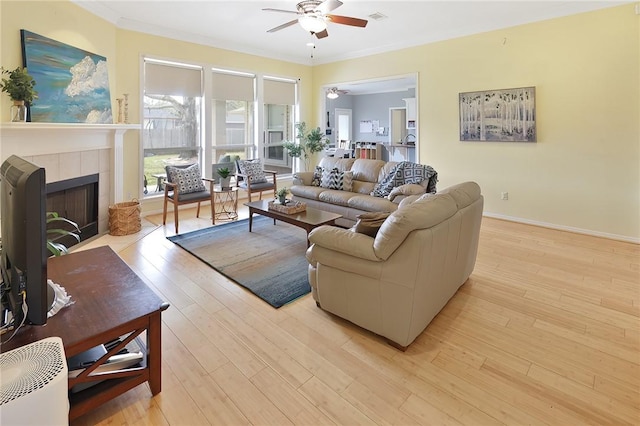 living room with ceiling fan, light wood-style flooring, visible vents, a tiled fireplace, and crown molding