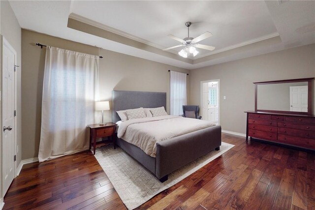 bedroom featuring a tray ceiling, wood-type flooring, crown molding, and baseboards