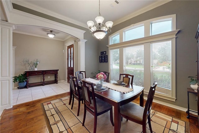 dining area with decorative columns, light wood-style floors, arched walkways, crown molding, and a chandelier