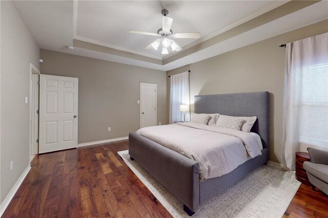 bedroom with a tray ceiling, wood finished floors, baseboards, and a ceiling fan