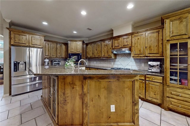 kitchen with stainless steel refrigerator with ice dispenser, under cabinet range hood, crown molding, an island with sink, and decorative backsplash
