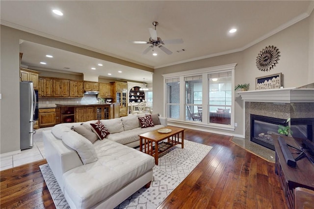 living area featuring ceiling fan, light wood-style floors, a high end fireplace, crown molding, and recessed lighting