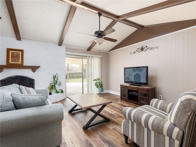 living room with ceiling fan, vaulted ceiling with beams, wood walls, light hardwood / wood-style floors, and a textured ceiling