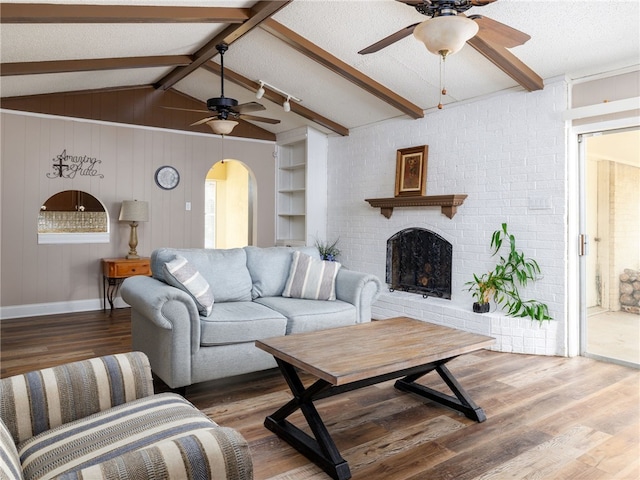 living room featuring hardwood / wood-style floors, vaulted ceiling with beams, built in features, a fireplace, and a textured ceiling