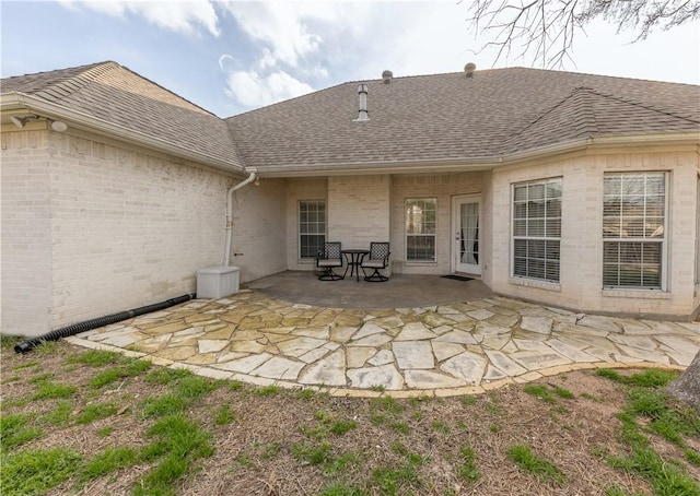 back of property with brick siding, roof with shingles, and a patio area