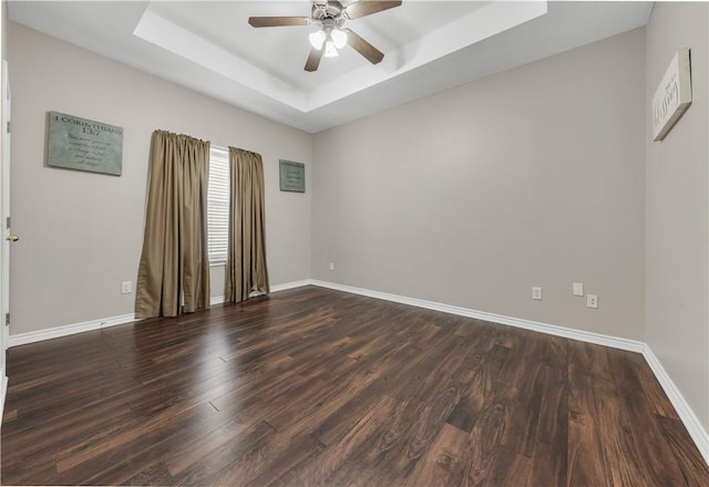 empty room with a tray ceiling, dark wood finished floors, and baseboards