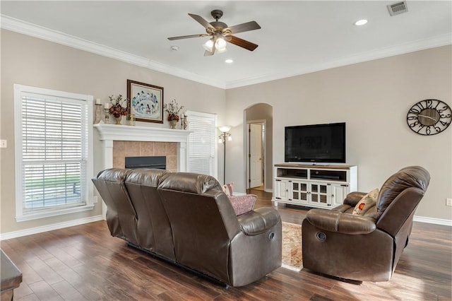 living room featuring ornamental molding, dark wood-style flooring, visible vents, and a tiled fireplace