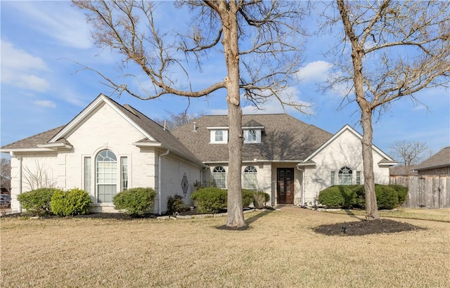 french country home featuring roof with shingles, fence, and a front yard