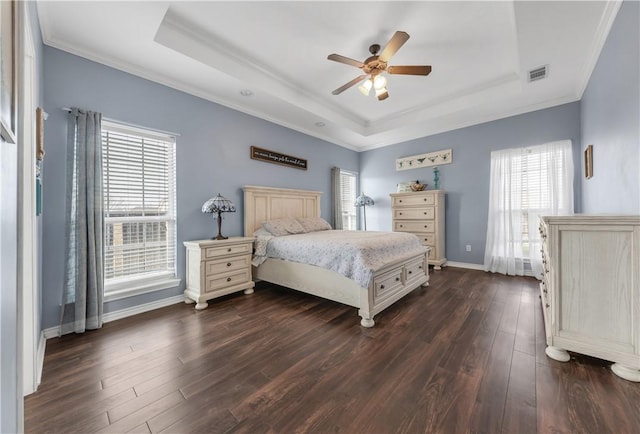 bedroom with dark wood-type flooring, visible vents, baseboards, a tray ceiling, and crown molding