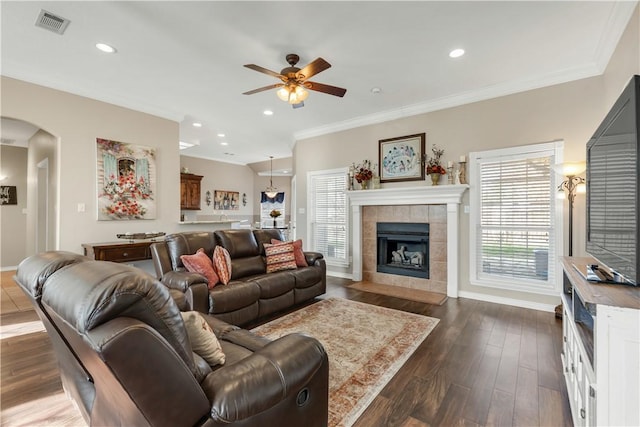 living room featuring arched walkways, a fireplace, baseboards, ornamental molding, and dark wood finished floors